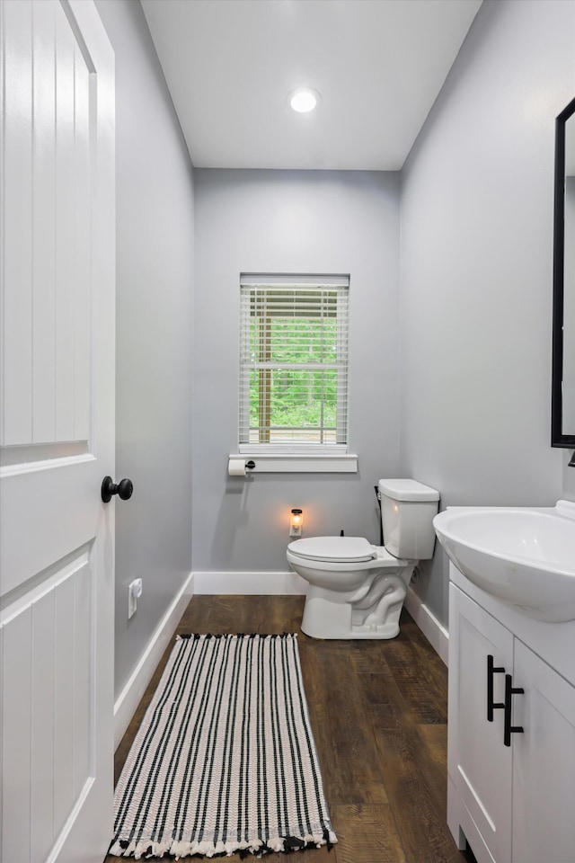 bathroom with baseboards, toilet, wood finished floors, vanity, and recessed lighting