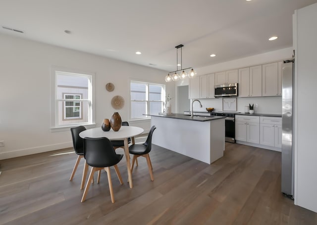 kitchen with dark countertops, a sink, appliances with stainless steel finishes, and dark wood-style floors