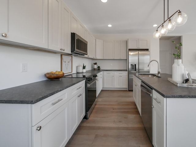kitchen with recessed lighting, a sink, light wood-style floors, dark countertops, and stainless steel appliances