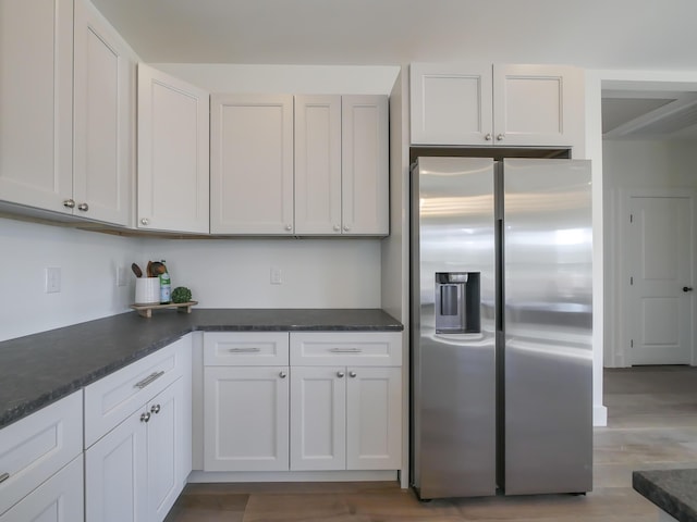 kitchen with dark countertops, white cabinets, stainless steel refrigerator with ice dispenser, and wood finished floors