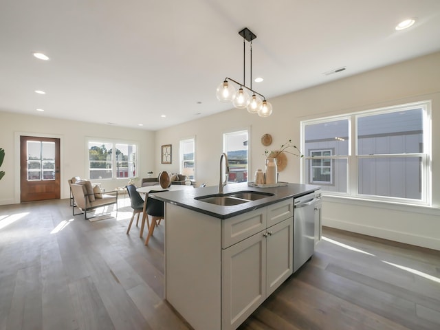 kitchen featuring an island with sink, a sink, dark countertops, visible vents, and dishwasher