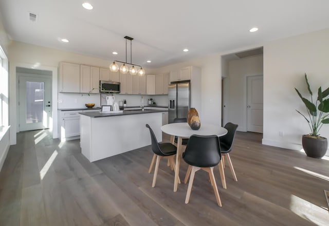 kitchen with dark wood-type flooring, visible vents, a center island with sink, dark countertops, and appliances with stainless steel finishes
