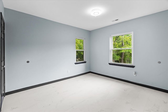 empty room with baseboards, a wealth of natural light, marble finish floor, and visible vents