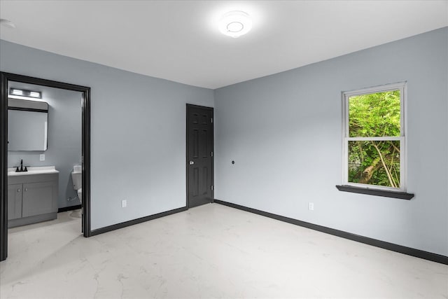 unfurnished bedroom with baseboards, marble finish floor, ensuite bath, and a sink