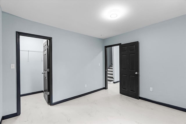 unfurnished bedroom featuring baseboards, marble finish floor, and a walk in closet