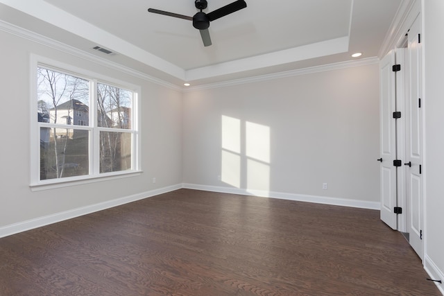 empty room with a raised ceiling, ceiling fan, dark wood-type flooring, baseboards, and ornamental molding