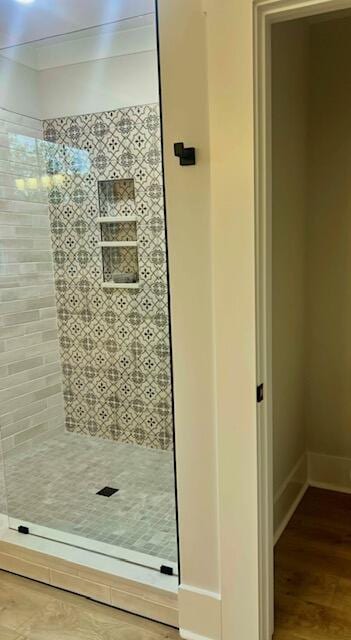 bathroom with a shower stall, wood finished floors, baseboards, and ornamental molding