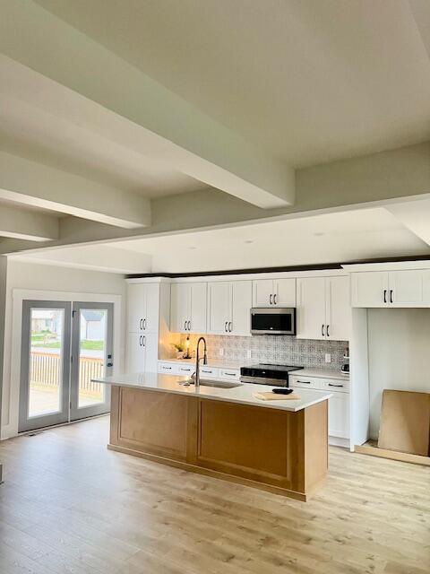 kitchen with stainless steel appliances, beam ceiling, a center island with sink, light wood finished floors, and white cabinets