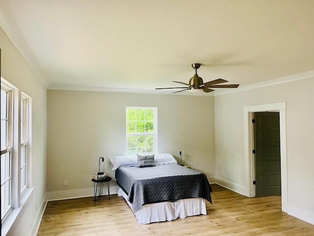 bedroom featuring crown molding, light wood-type flooring, baseboards, and ceiling fan
