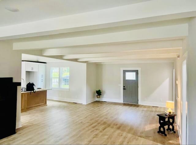 unfurnished living room with baseboards, light wood-style flooring, and beam ceiling