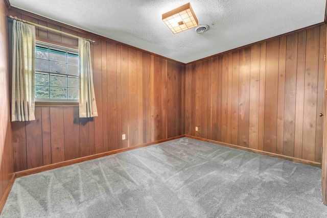 carpeted empty room featuring a textured ceiling and wood walls