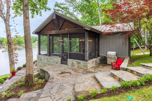 rear view of property featuring a standing seam roof, metal roof, a patio, a water view, and a sunroom