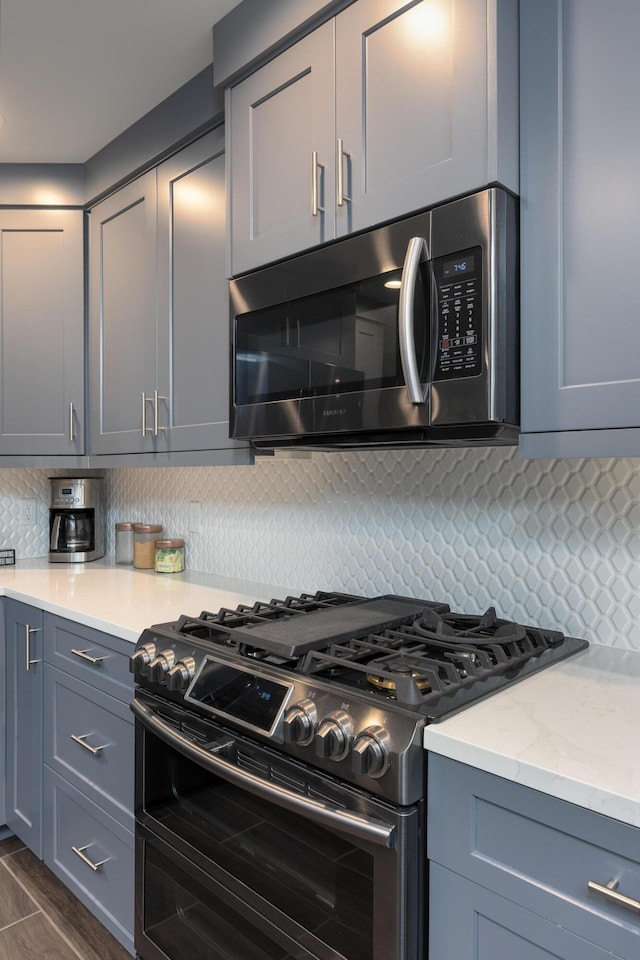 kitchen with appliances with stainless steel finishes, gray cabinets, and tasteful backsplash