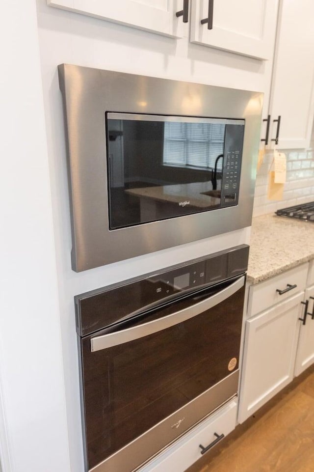 8880 Knolling Loop Unit 35, Ooltewah, TN 37363 - kitchen view of built in microwave, oven, white cabinetry, decorative backsplash, and light stone countertops