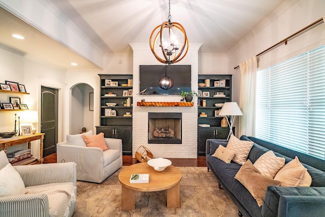 living room featuring crown molding, wood finished floors, a brick fireplace, arched walkways, and a chandelier