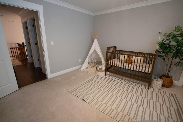 carpeted bedroom with baseboards, ornamental molding, and a nursery area