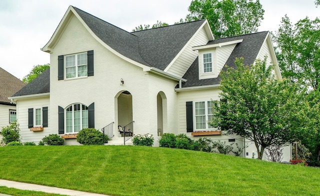 view of front of property featuring a shingled roof, brick siding, and a front lawn