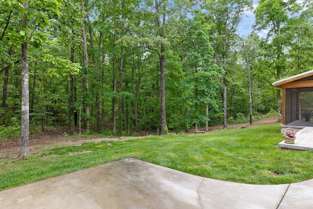 view of grassy yard with a patio area, a sunroom, and a view of trees