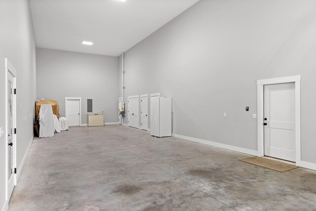 unfurnished room featuring concrete flooring, a towering ceiling, and baseboards