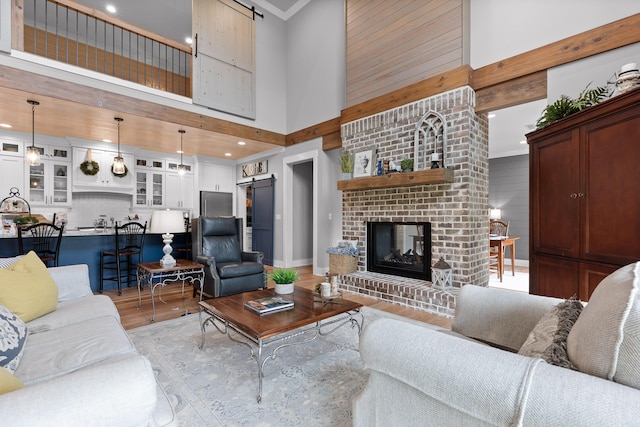 living area with a barn door, a high ceiling, light wood-type flooring, a brick fireplace, and ornamental molding