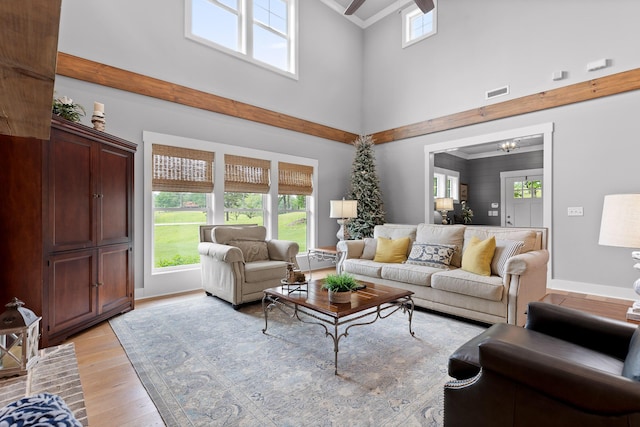 living room featuring a towering ceiling, light wood-style flooring, a chandelier, baseboards, and ornamental molding