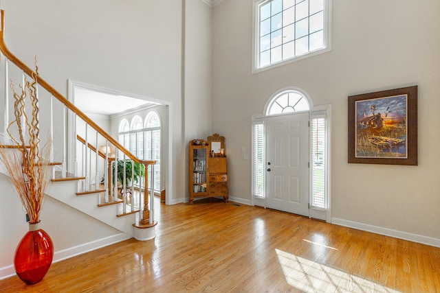 foyer with a towering ceiling, stairs, wood finished floors, baseboards, and crown molding