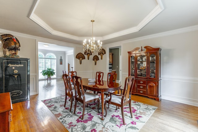 dining area with a chandelier, ornamental molding, light wood-type flooring, and wainscoting