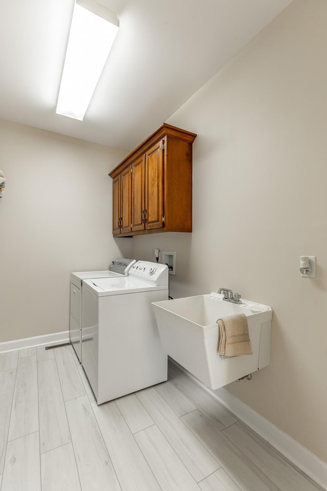 clothes washing area with washer and dryer, cabinet space, baseboards, and wood finish floors