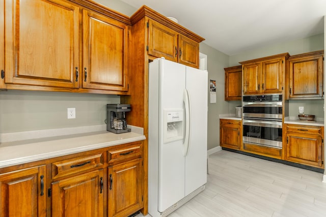 kitchen featuring white refrigerator with ice dispenser, double oven, brown cabinetry, and light countertops