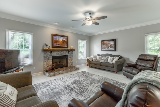 living room with ceiling fan, crown molding, wood finished floors, a stone fireplace, and baseboards
