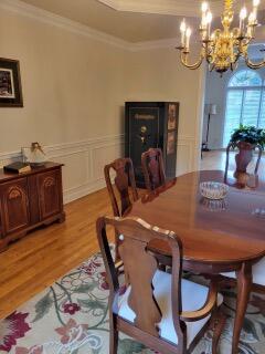 dining area with a chandelier, light wood-style flooring, crown molding, a raised ceiling, and wainscoting