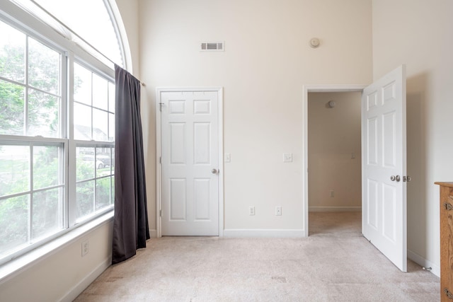 unfurnished bedroom featuring light colored carpet, a towering ceiling, and baseboards