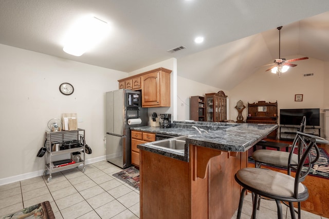 kitchen featuring freestanding refrigerator, a peninsula, dark countertops, a kitchen bar, and a ceiling fan