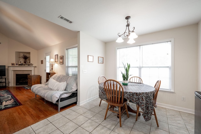 dining room with baseboards, light tile patterned floors, a chandelier, a fireplace, and vaulted ceiling