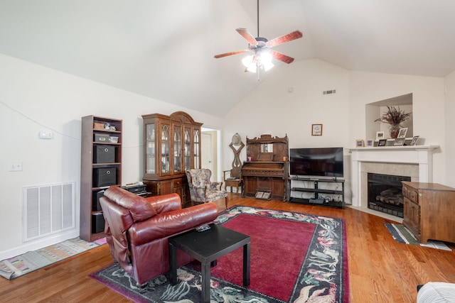 living area featuring lofted ceiling, a ceiling fan, a fireplace with flush hearth, and wood finished floors