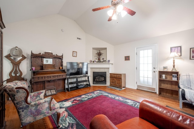 living room with ceiling fan, vaulted ceiling, wood finished floors, and a tile fireplace