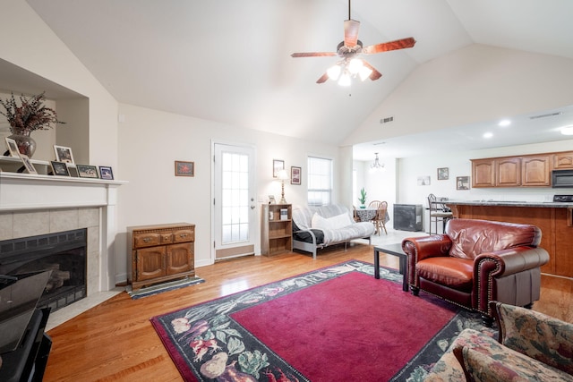 living room featuring light wood-style flooring, a ceiling fan, a tile fireplace, and high vaulted ceiling