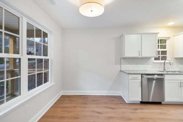 kitchen featuring stainless steel dishwasher, a sink, light stone counters, backsplash, and light wood-type flooring