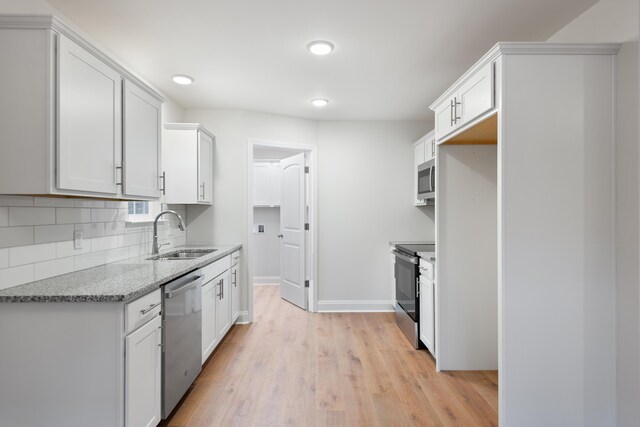 kitchen featuring a sink, stainless steel appliances, decorative backsplash, light wood finished floors, and baseboards
