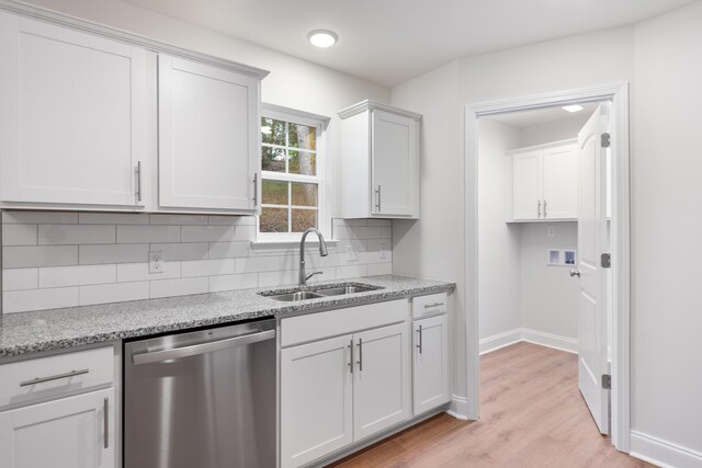 kitchen with stainless steel dishwasher, a sink, light wood-style floors, decorative backsplash, and baseboards