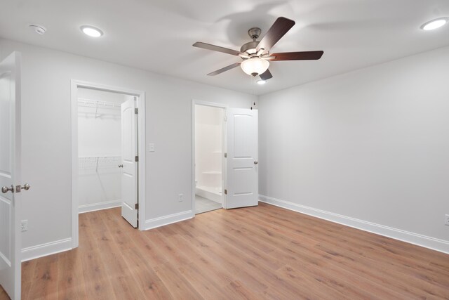 unfurnished bedroom featuring a spacious closet, light wood-style flooring, baseboards, a closet, and ceiling fan