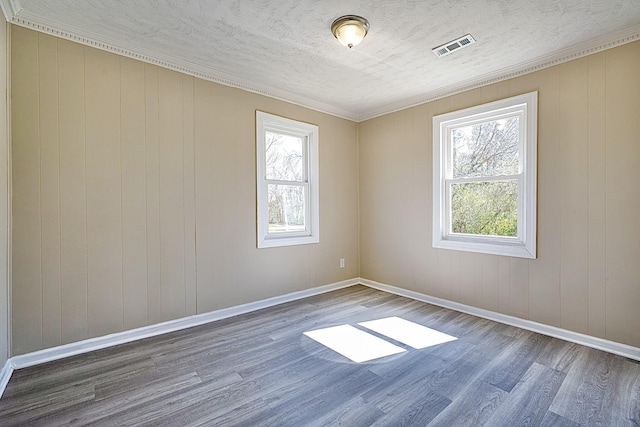 unfurnished room featuring healthy amount of natural light, wood finished floors, baseboards, crown molding, and a textured ceiling