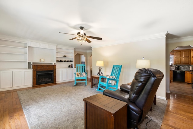 living area with arched walkways, ceiling fan, ornamental molding, a fireplace, and wood finished floors