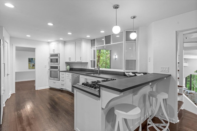 kitchen featuring dark countertops, a sink, stainless steel appliances, white cabinetry, and dark wood-type flooring