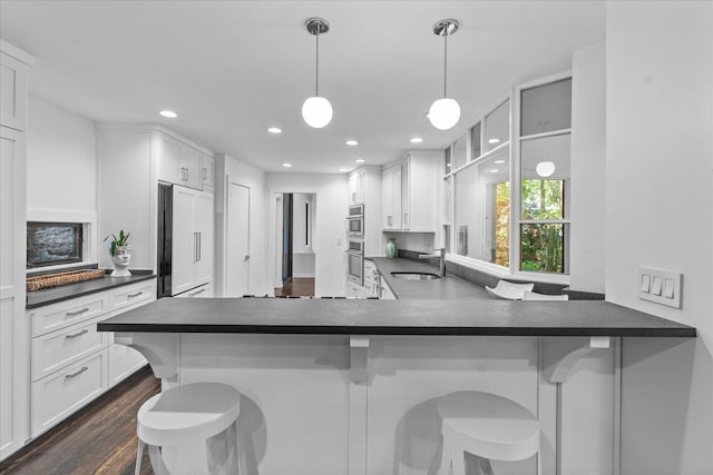 kitchen featuring dark countertops, a sink, paneled built in refrigerator, white cabinetry, and recessed lighting