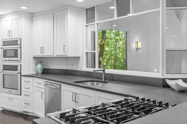 kitchen with a sink, appliances with stainless steel finishes, dark countertops, white cabinetry, and recessed lighting