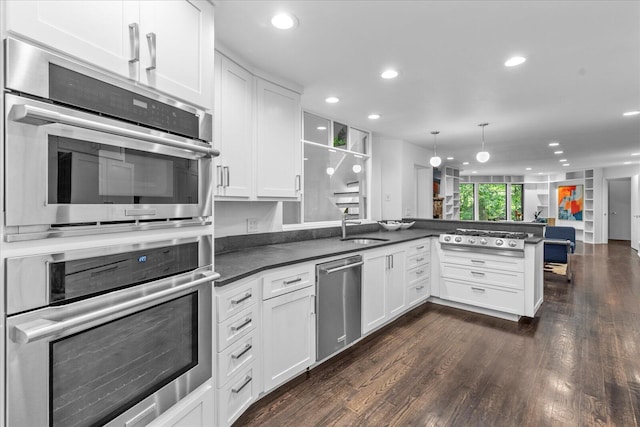 kitchen with stainless steel appliances, a peninsula, a sink, dark countertops, and white cabinets