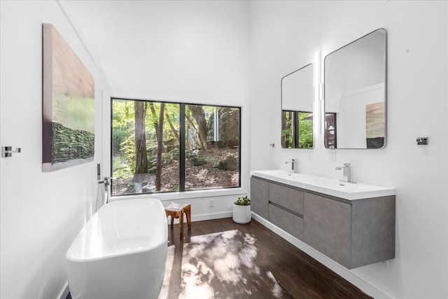 full bathroom featuring wood finished floors, a soaking tub, baseboards, and double vanity