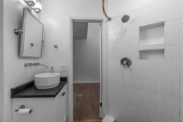 full bathroom with a tile shower, vanity, and wood finished floors
