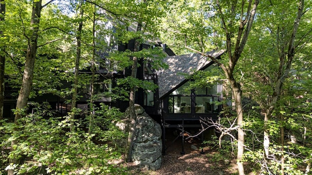 view of home's exterior with roof with shingles, a sunroom, and a chimney
